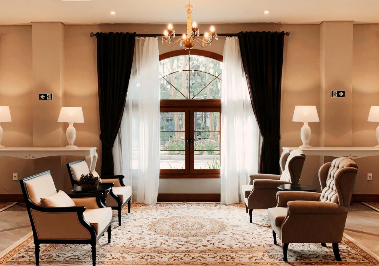 Buona Vitta Gramado Resort & Spa By Gramado Parks Kültér fotó The photo shows an elegantly styled living room. There are two armchairs and a sofa arranged comfortably around an intricate area rug. Large windows are adorned with sheer white curtains and dark curtains, allowing natural light to fill the space. A 
