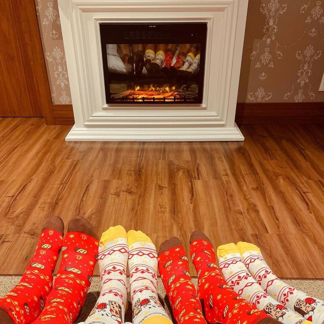 Buona Vitta Gramado Resort & Spa By Gramado Parks Kültér fotó The photo shows a cozy indoor setting with a warm fireplace. In the foreground, several pairs of feet are displayed, each wearing brightly colored socks with various patterns. The socks include red, yellow, and white designs, contributing to a cheerf