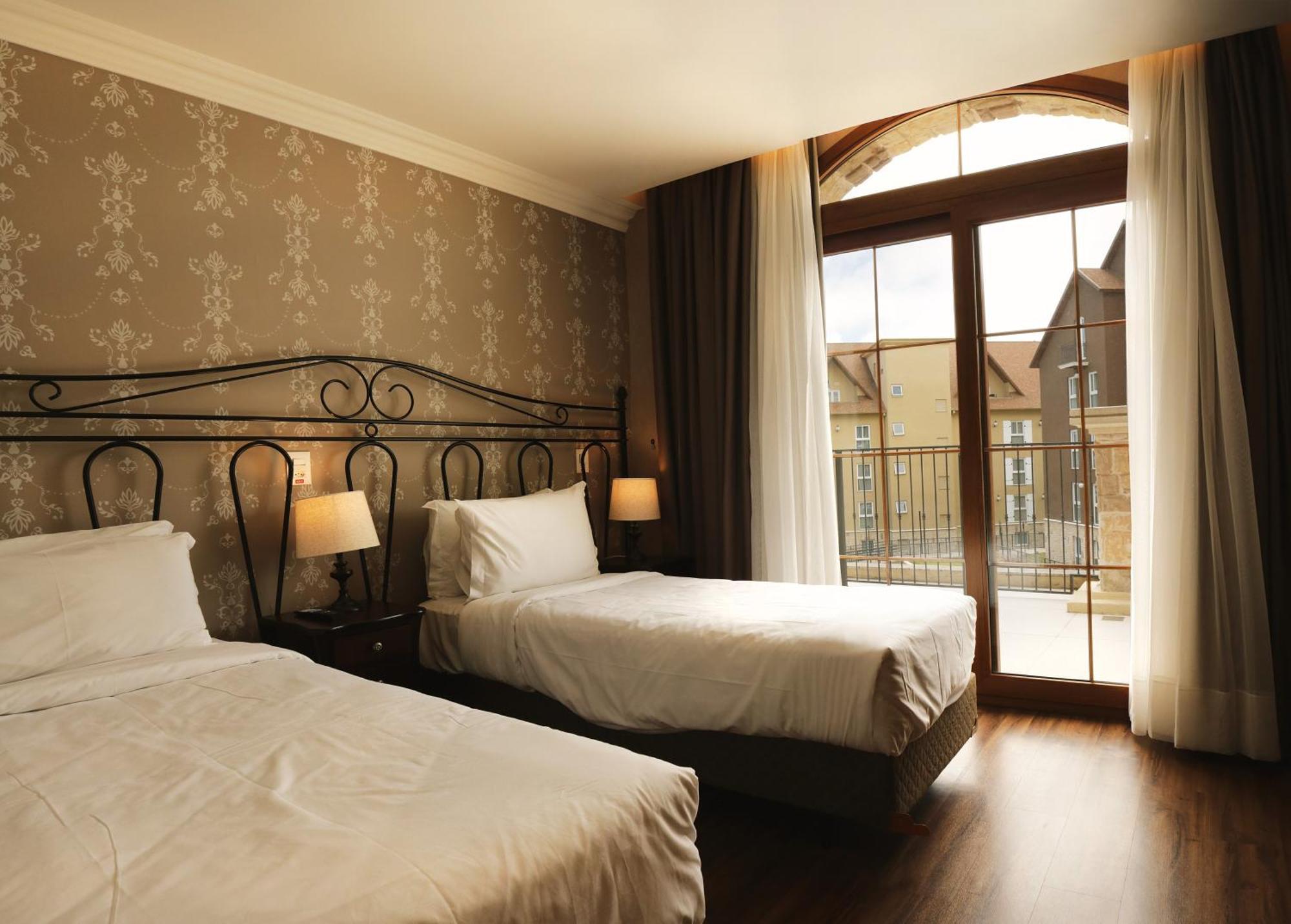 Buona Vitta Gramado Resort & Spa By Gramado Parks Kültér fotó The photo shows a well-decorated hotel room featuring two beds. One bed is larger, likely a double bed, while the other is a single bed. The walls are adorned with a floral pattern, and there are bedside lamps next to the larger bed. Large windows wi