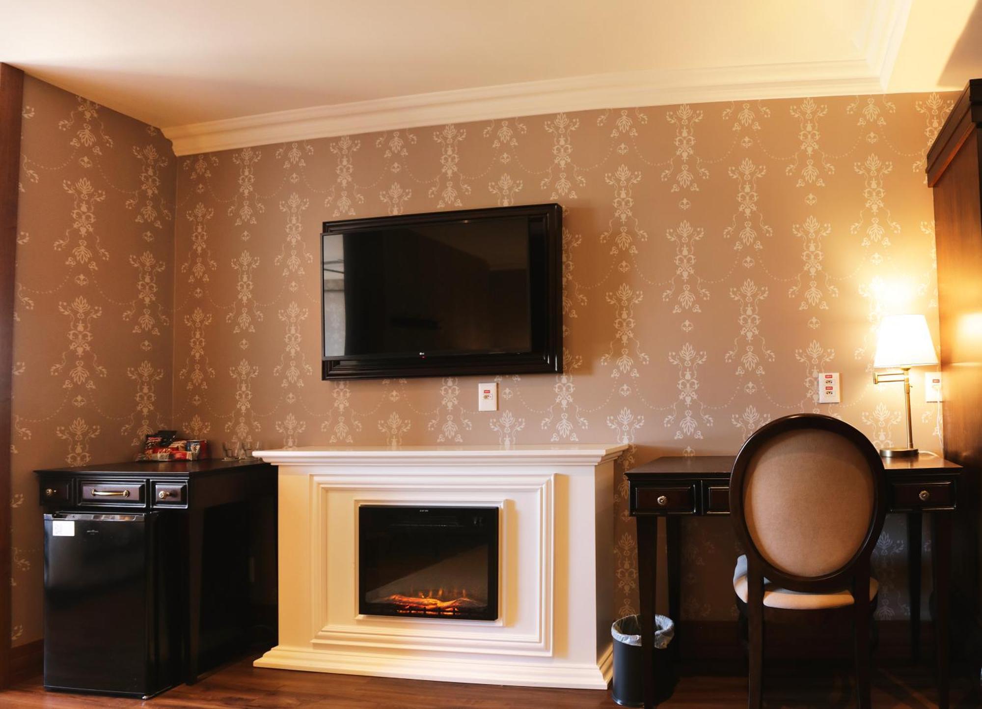 Buona Vitta Gramado Resort & Spa By Gramado Parks Kültér fotó The photo shows a cozy room featuring a decorative wall with a subtle pattern. On one side, there is a modern flat-screen television mounted on the wall. Below it, there is a stylish electric fireplace framed in white. Adjacent to the fireplace is a 
