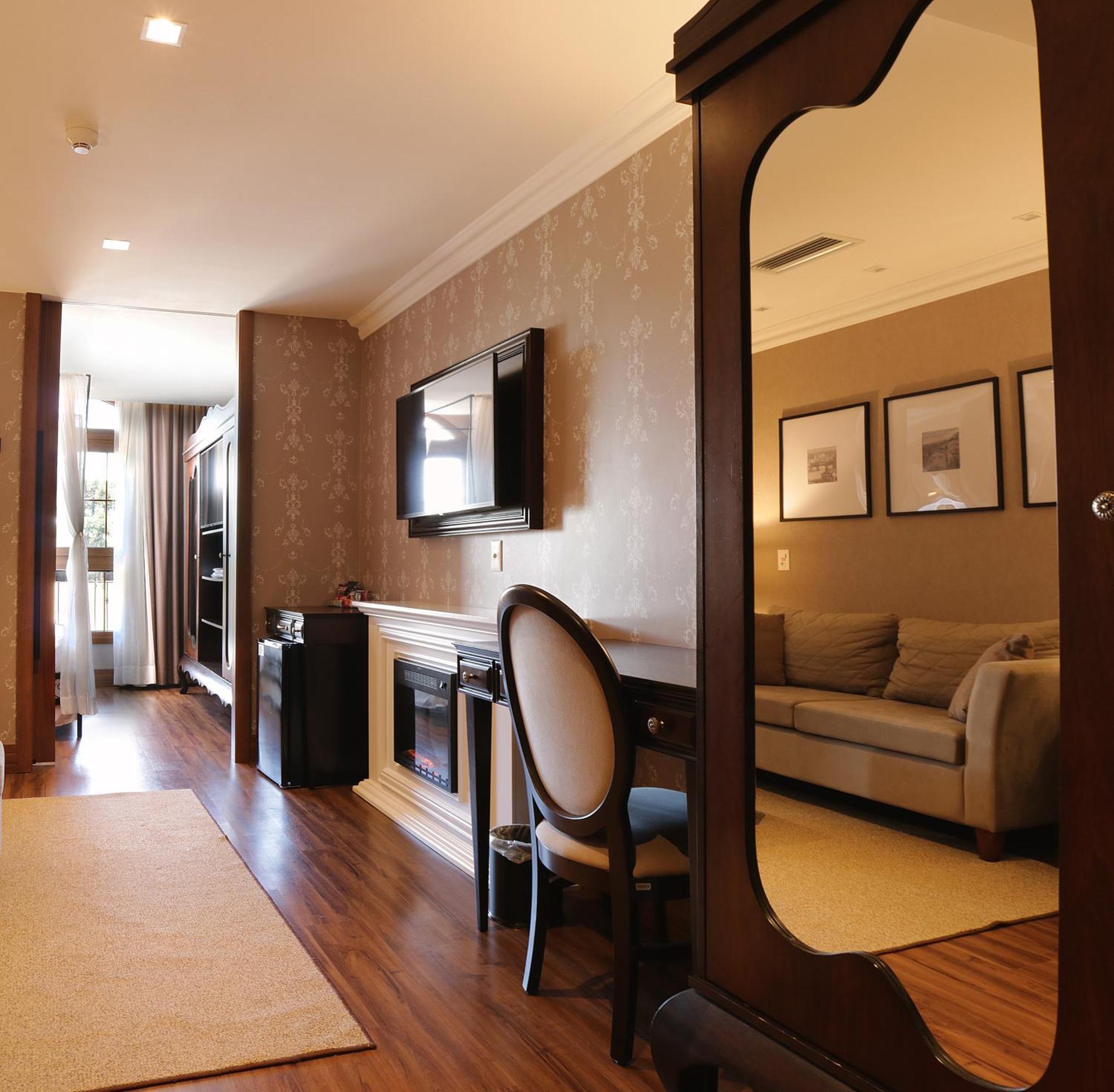 Buona Vitta Gramado Resort & Spa By Gramado Parks Kültér fotó The photo shows a well-decorated room that appears to be a living area or a hotel suite. In the foreground, there is a round chair and a desk. A large mirror reflects the living space, creating a sense of spaciousness. 

On the wall is a flat-screen 