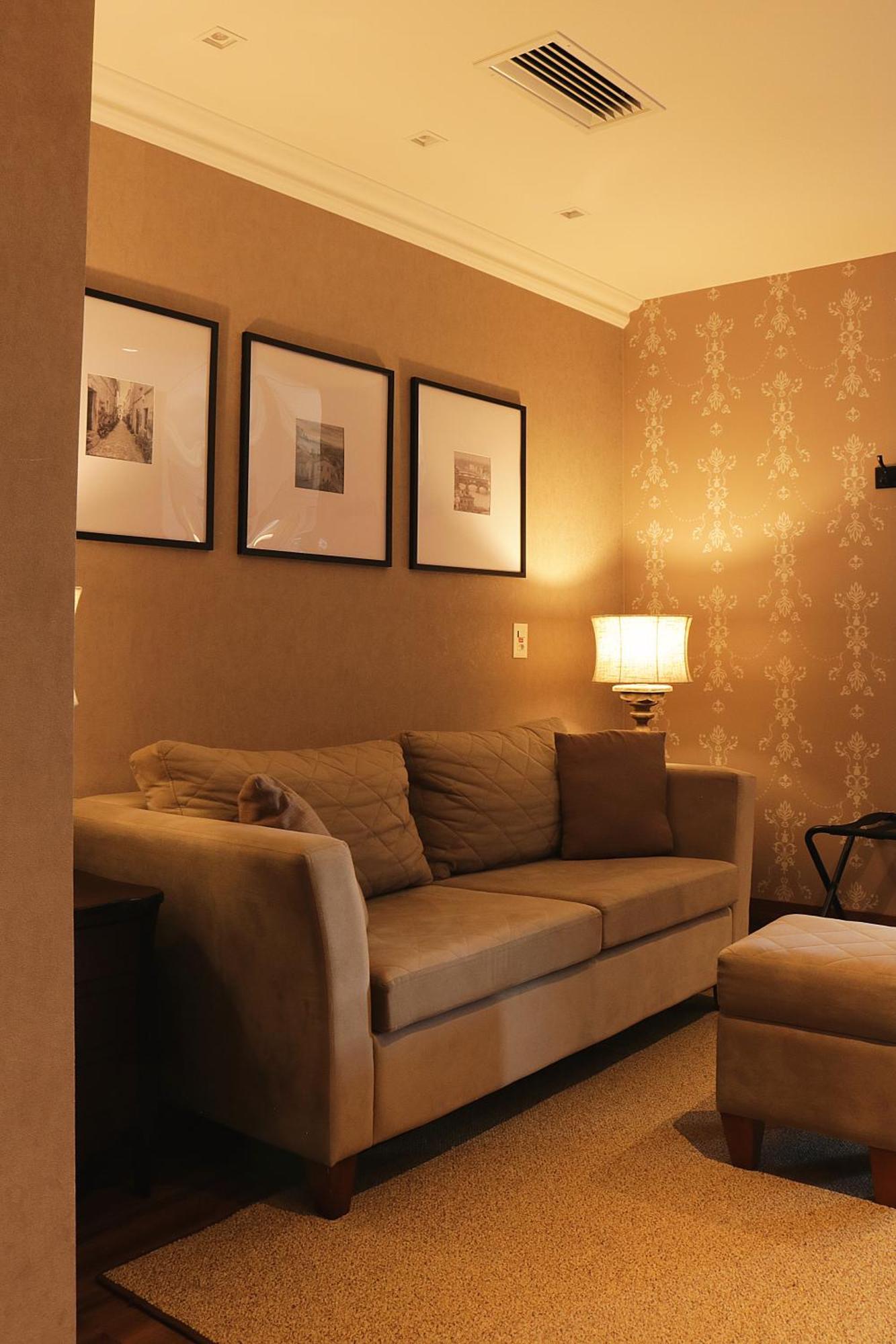Buona Vitta Gramado Resort & Spa By Gramado Parks Kültér fotó The photo shows a cozy living room setting. There is a light-colored sofa adorned with several cushions, positioned against a wall that has a subtle pattern. Above the sofa, there are three framed artworks or photographs hanging on the wall. To the s