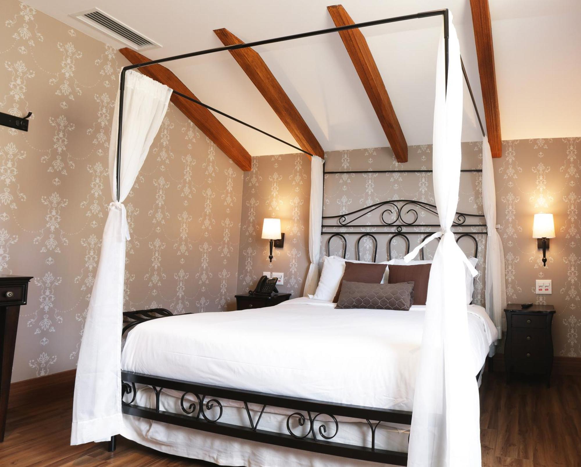 Buona Vitta Gramado Resort & Spa By Gramado Parks Kültér fotó The photo shows a beautifully designed bedroom featuring a four-poster bed with a metal frame and flowing white curtains. The bed is adorned with white bedding and brown decorative pillows. The room has wooden beams on the ceiling and is decorated wi